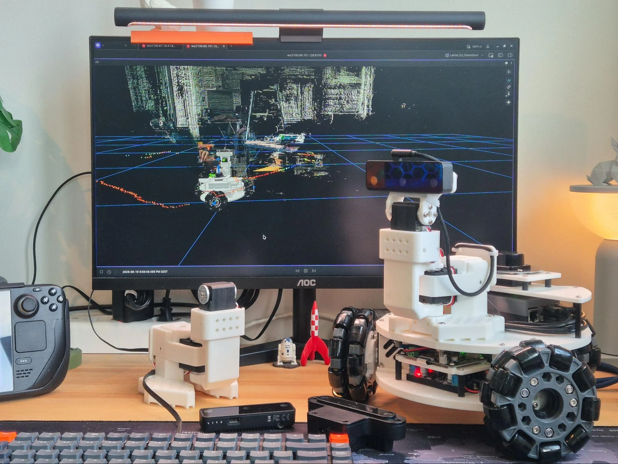 The LeKiwi robot with its OAK-D S2 pan-tilt camera on a desk, next to a monitor showing a pointcloud in Foxglove and a Steam Deck